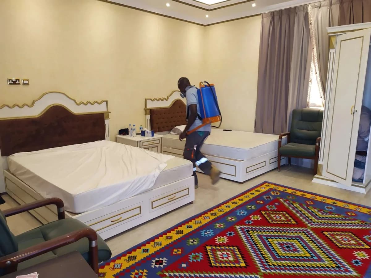 Technician with a backpack sprayer and respirator treating a bedroom